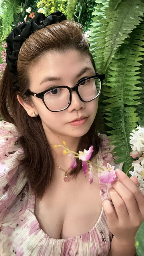 my pic 3 Hailey Khoo Academy founder Hailey Khoo holding a flower plant wearing thick black glasses with plant as a background with flower dress at AIA All Stars Annual Award