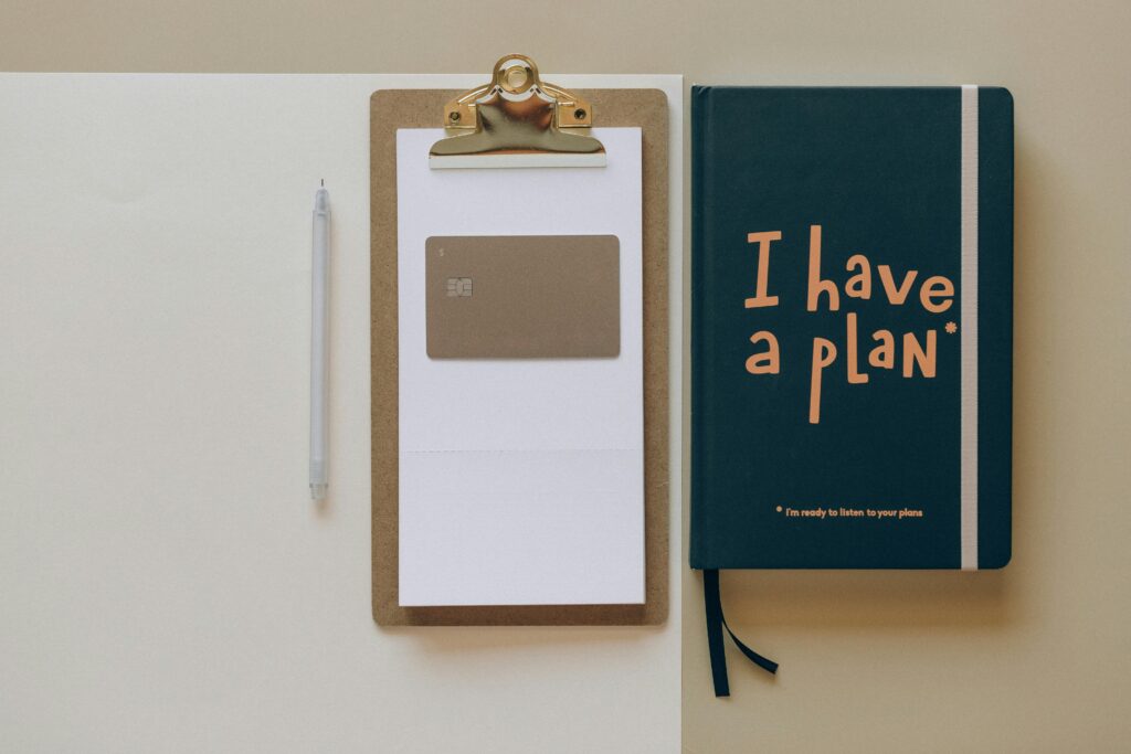 financial planning course A minimalist office setup featuring a planner, clipboard, card, and pen, perfect for planning and organization.